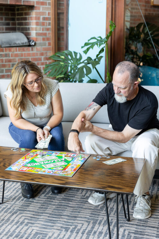 older man shown playing a money based board game with a female minds matter consultant on a couch