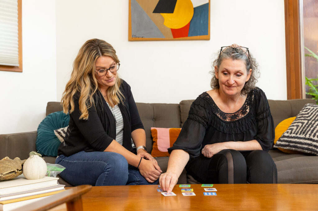 woman sitting on couch is shown playing a memory card game on a table with a minds matter consultant